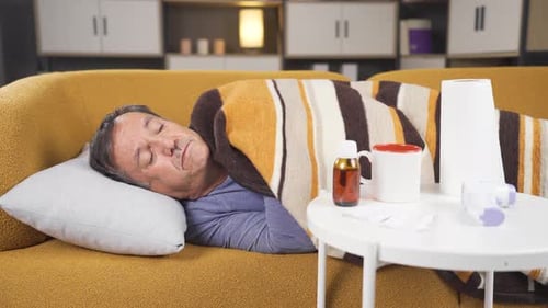 Man Under Blanket Lays on Couch at Home