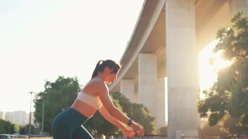 Woman Doing Squats Near Bridge at City Park During Sunrise