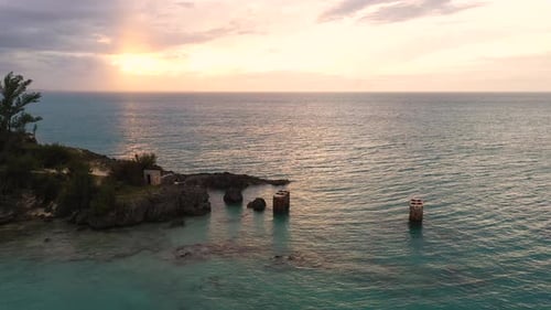 Aerial view of old bridge mounts in clear turquoise water by tropical island. Sunset over big ocean.