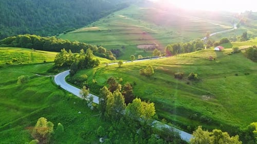 A Road Passes Hills Covered with Spruce Forests and Meadows Against a Cloudy Sky