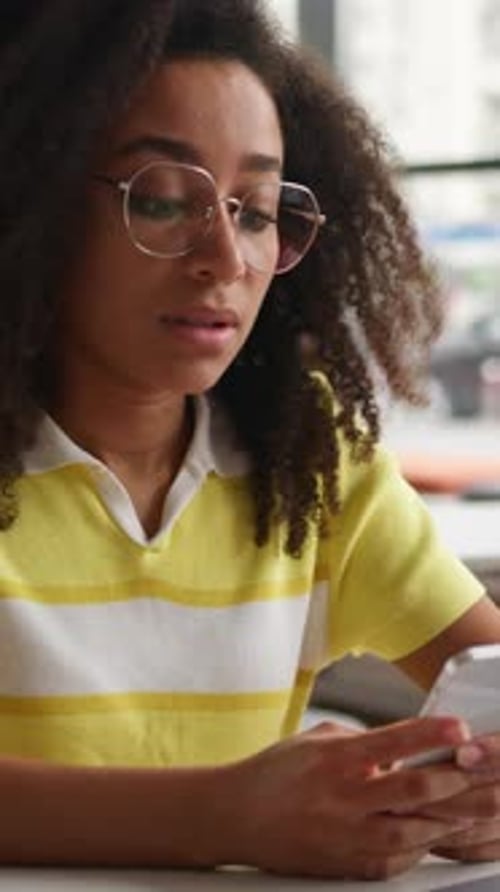 Hesitate Dreamy African American Girl Holding Mobile Phone Thinking at Table Relaxing After Studying