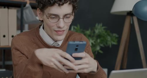 Portrait of Young Man Using Smartphone Surfing Internet and Smiling in Office