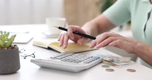 Woman Calculating Finances at Desk with Calculator and Notebook