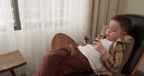 Boy Playing Mobile Game Reclined in Chair