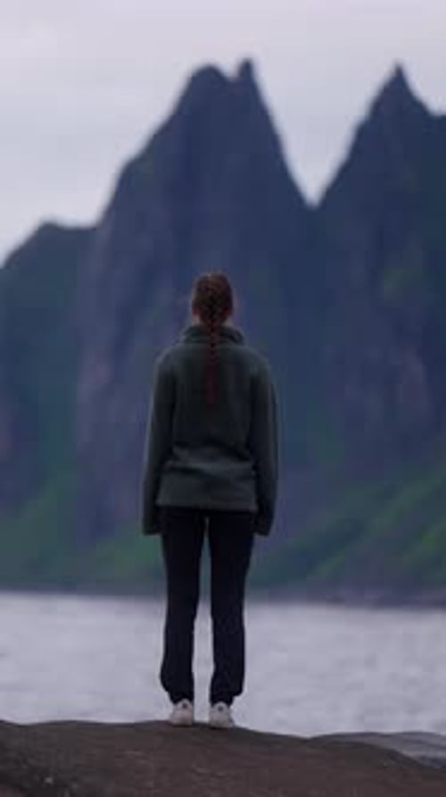 Woman stands at Senja cliffs, Devil’s Teeth, under looming rock formations