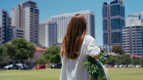 Mujer que lleva productos frescos en una bolsa de malla mientras camina por un parque de la ciudad