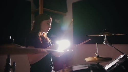 Woman Plays Drums in Studio with Dramatic Lighting