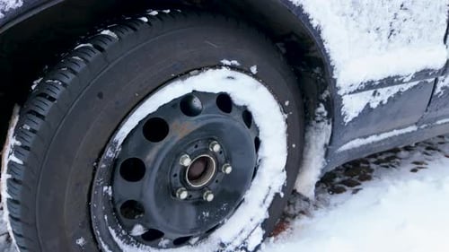 Close-up of a car tire partially covered in snow, showcasing winter conditions and icy roads