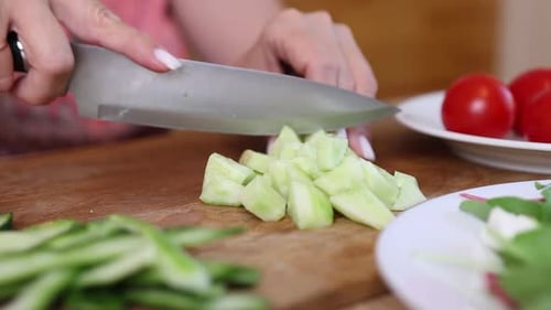 05 1Woman cutting cucumber into cubes on wooden board near tomatoes and salad plate with fresh veget