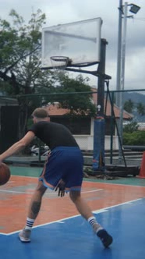 vertical video, view from the back of a man playing basketball in the park