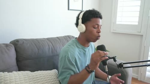 Homme afro-américain répondant à un signal d'ordinateur portable, parlant dans un microphone dans le salon sur un canapé gris