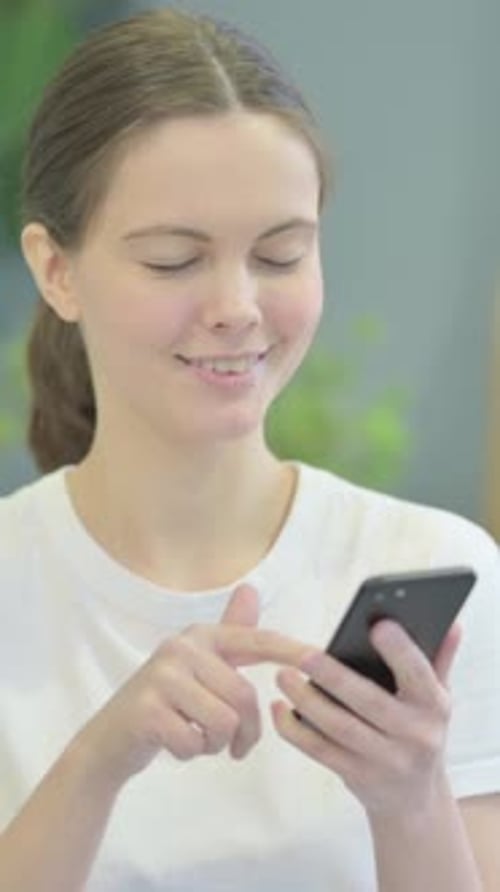 Smiling Young Woman Using Mobile Phone Indoors