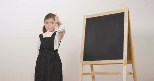 A happy girl dressed as a teacher in front of a small blackboard holds her arms folded and smiles.