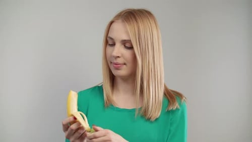 Close Of Blond Woman Eating Banana At White Background. Portrait Of Blonde Girl Biting Ripe Fruit...