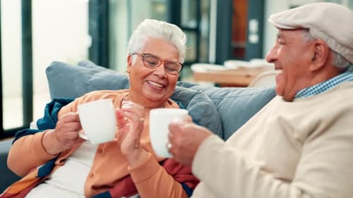 Senior Couple Toasting with Mugs on Living Room Sofa