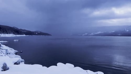 Slow pan over dramatic dark moody Upper Arrow Lake British Columbia covered in snow and revealing th