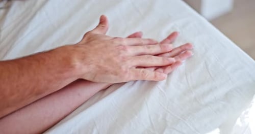 Couple Holding Hands Intimately on Bed Sheet