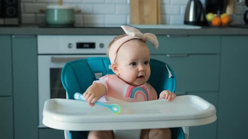 Adorable Baby with Spoon in High Chair at Home