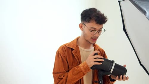 Young Asian Man Photographer Setting Up And Adjusting His Professional Studio Lighting Equipment