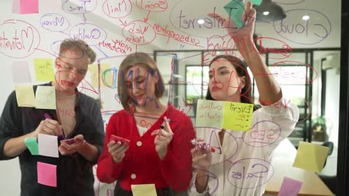 Team Brainstorming Ideas Writing on Clear Board in Office