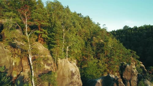 Das Licht des Sonnenuntergangs beleuchtet schroffe Steinfelsen, die von dichtem Wald umgeben sind, und sorgen für eine idyllische und erholsame Atmosphäre