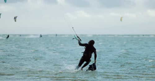 Kitesurfer starting his session, jumping onto kiteboard on blue flat water