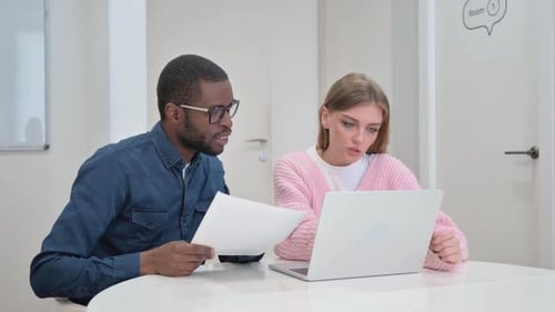 Two Professionals Collaborating Over Laptop in Modern Office