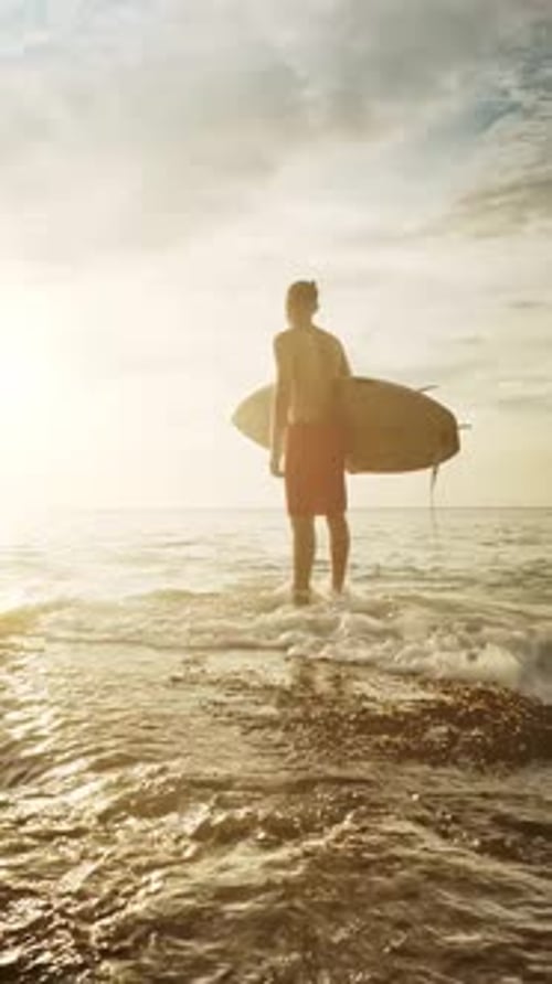 Surfer Standing on Reef with Surfboard at Sunset Waiting for Waves