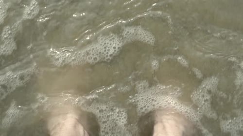 Waves rushing over bare feet on sandy beach in slow motion