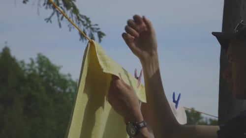 Man Removing Clothespins And Dry Towel From The Clothesline Outdoor - close up slowmo