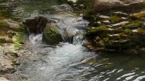 Relaxing close up of clear fresh water flowing over stones down a brook with more moss covered stone