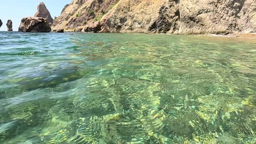Sea Water Surface Camera Flies Over the Calm Azure Sea with Volcanic Rocky Shores on Background