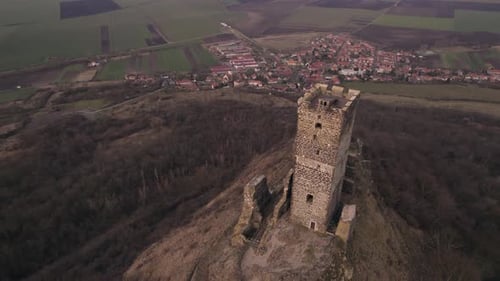 Orbiting view drone, hilltop medieval castle tower ruins with village below