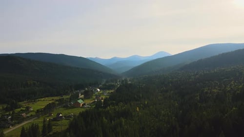 Aerial View of Bright Foggy Morning Over Small Rural Homes Between Dark Peaks with Mountain Forest