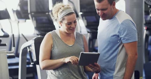 Woman Showing Tablet to Man in Modern Gym