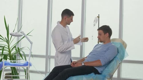 A Male Doctor Puts an IV Drip on AaPatient Sitting on a Couch in the Office
