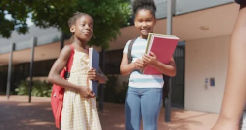 Video of three happy diverse schoolchildren with schoolbags greeting outside school