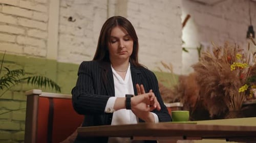 Una mujer de negocios mira nerviosamente el reloj inteligente de pulsera y suspira agarrándose la cabeza con la mano mientras