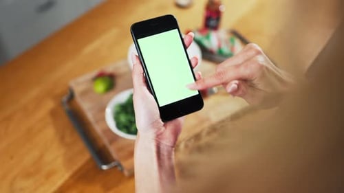 Close up shot of woman hand holding green screen phone when cooking food in kitchen.