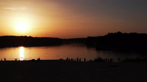 Aerial View of Silhouettes of People Who Swim and Relax on Lake Surrounded By Forest at Sunset