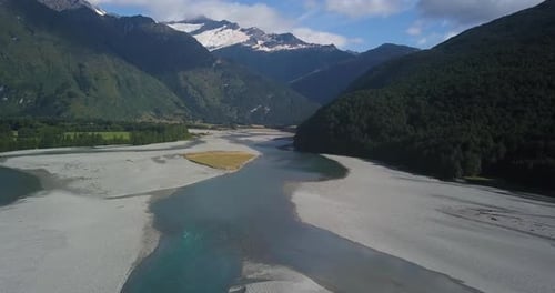 Ascending shot of an icy river thawing out on a sunny day, with an ice covered glacier in the distan