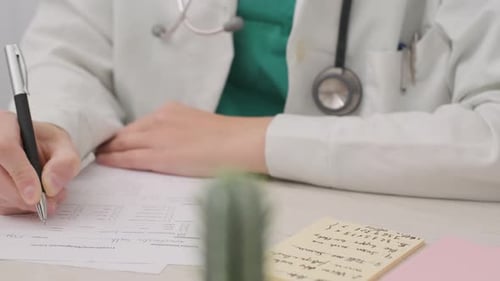 Physician Completing The Medical Report At The Table Inside The Doctor’s Office. medium shot