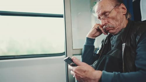 Vue rapprochée d'une personne âgée pensive utilisant un téléphone portable lors d'un voyage en train coupé
