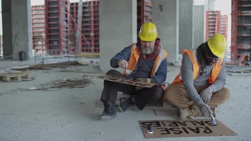Construction Workers Paint Protest Signs Indoors