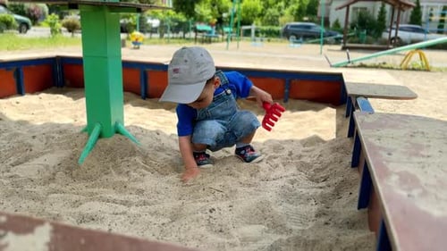 Un garçon caucasien enfonce une main dans le sable du bac à sable. L'enfant ratisse le sable d'une autre main
.