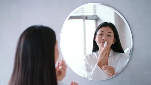 Woman Applying Lip Balm in Bathroom Mirror