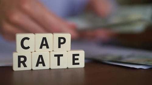 Concept of capitalization rate. Cape rate word with selective focus. Person counting cash on the bac