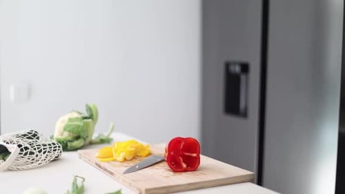 Man Cutting Red Pepper in Kitchen with Vegetables