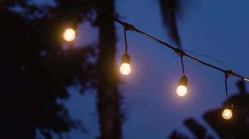 Little Light Bulbs String Hanging Against Evening Sky. Low Angle Shot