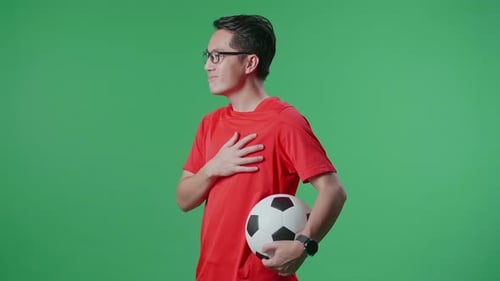 Side View Of Asian Man With A Ball Putting Hand On His Heart To Respect On Green Screen Background